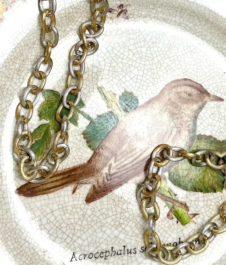 A gold and silver chain across an antique plate painted with a small bird